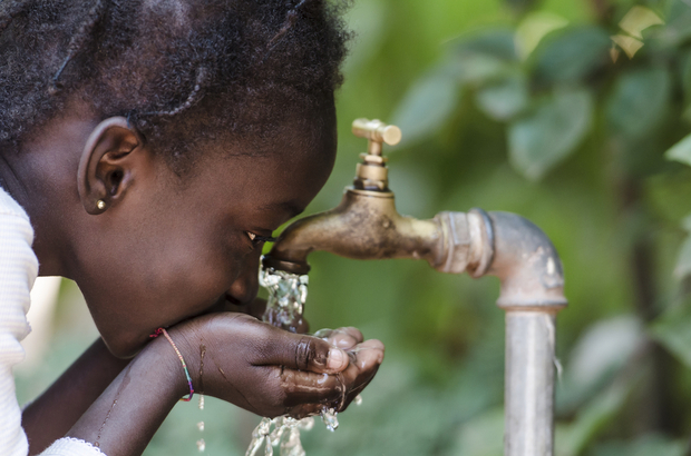 A young African girl drinking clean water from a tap A young African girl drinking clean water from a tap