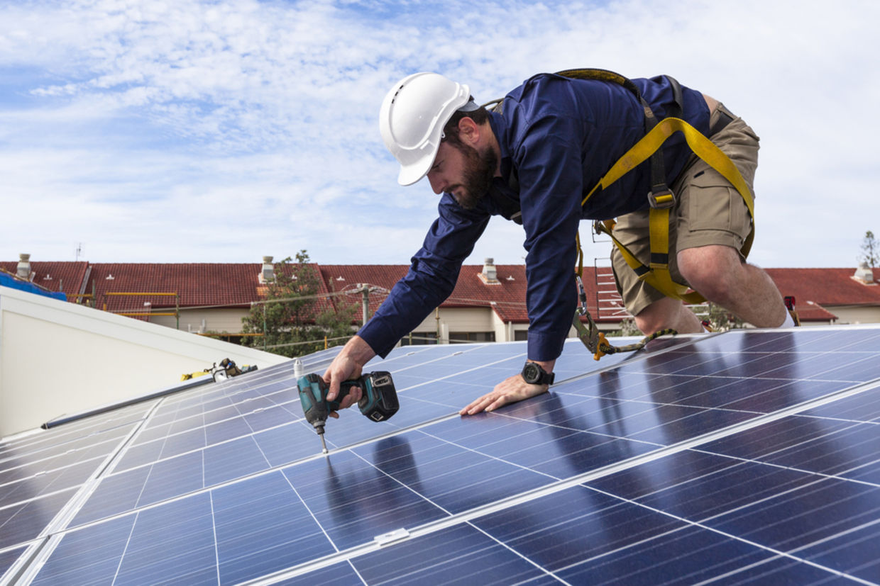 Solar panel technician with drill installing solar panels on roof Solar panel technician with drill installing solar panels on roof