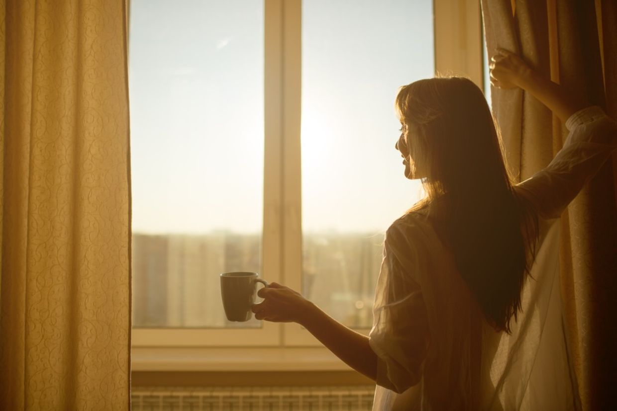 Woman in the morning. Attractive sexy woman with neat body is holding a cup with hot tea or coffee and looking at the sunrise standing near the window in her home and having a perfect cozy morning. Woman in the morning. Attractive sexy woman with neat body is holding a cup with hot tea or coffee and looking at the sunrise standing near the window in her home and having a perfect cozy morning.