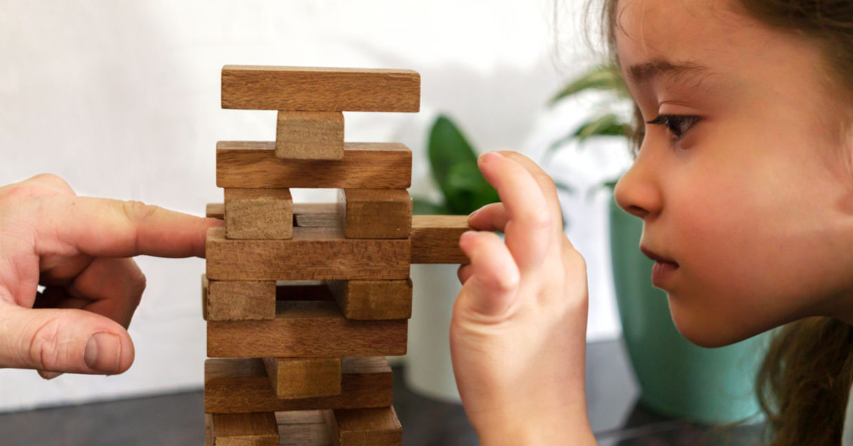 As a father and daughter play tumble tower, dad models resilience by assisting her in strengthening the tower. As a father and daughter play tumble tower, dad models resilience by assisting her in strengthening the tower.