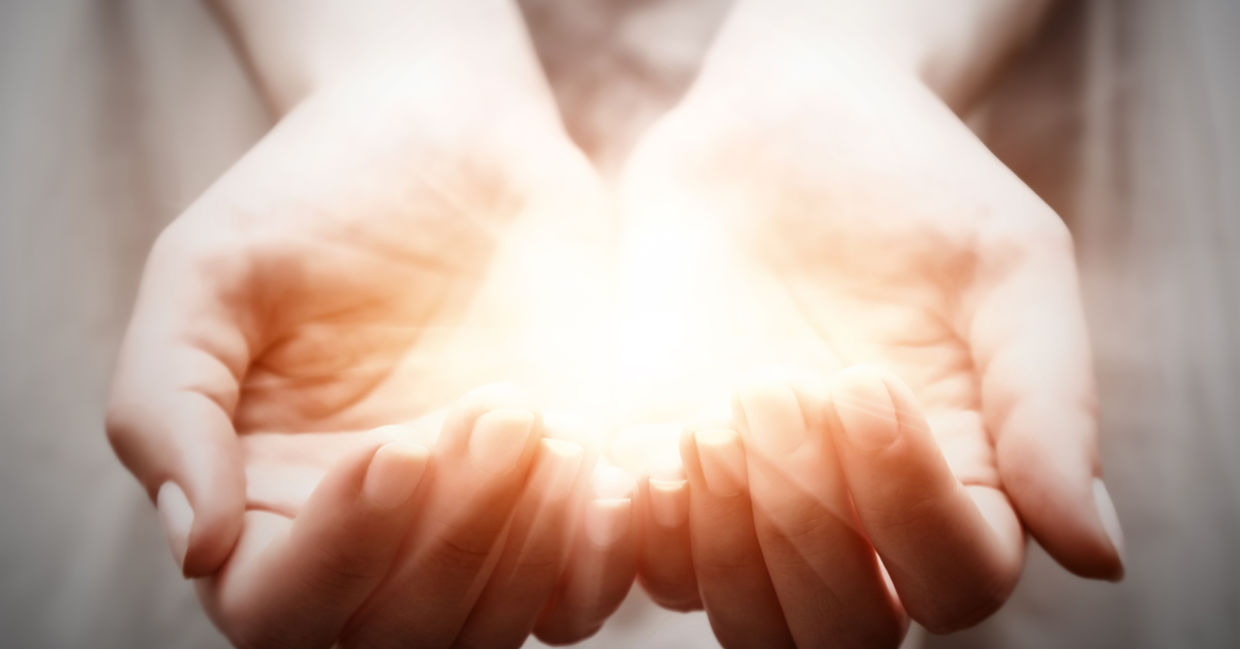 A woman cups light in her palms, representing giving and spirituality. A woman cups light in her palms, representing giving and spirituality.