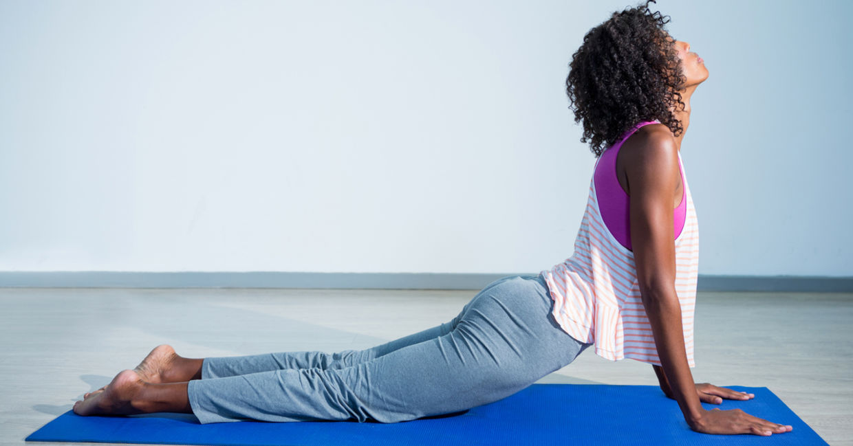Woman doing cobra yoga pose on exercise mat in gym.