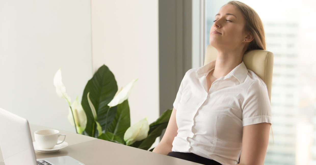 A woman sits comfortably at her desk and practices mindfulness. A woman sits comfortably at her desk and practices mindfulness.