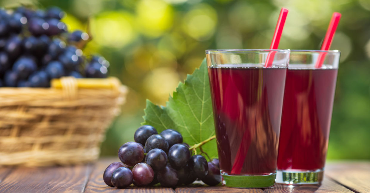 Bunches of purple grapes on a table beside two glasses of fresh grape juice. Bunches of purple grapes on a table beside two glasses of fresh grape juice.