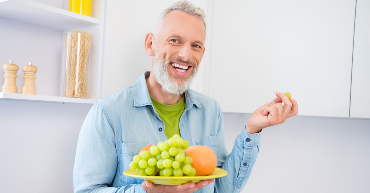A middle-aged man holds a plate of green grapes. A middle-aged man holds a plate of green grapes.