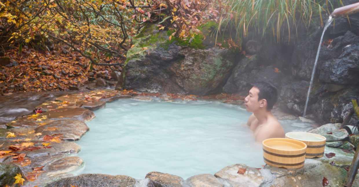 A man soaks in a mineral spring in a Japanese forest. A man soaks in a mineral spring in a Japanese forest.